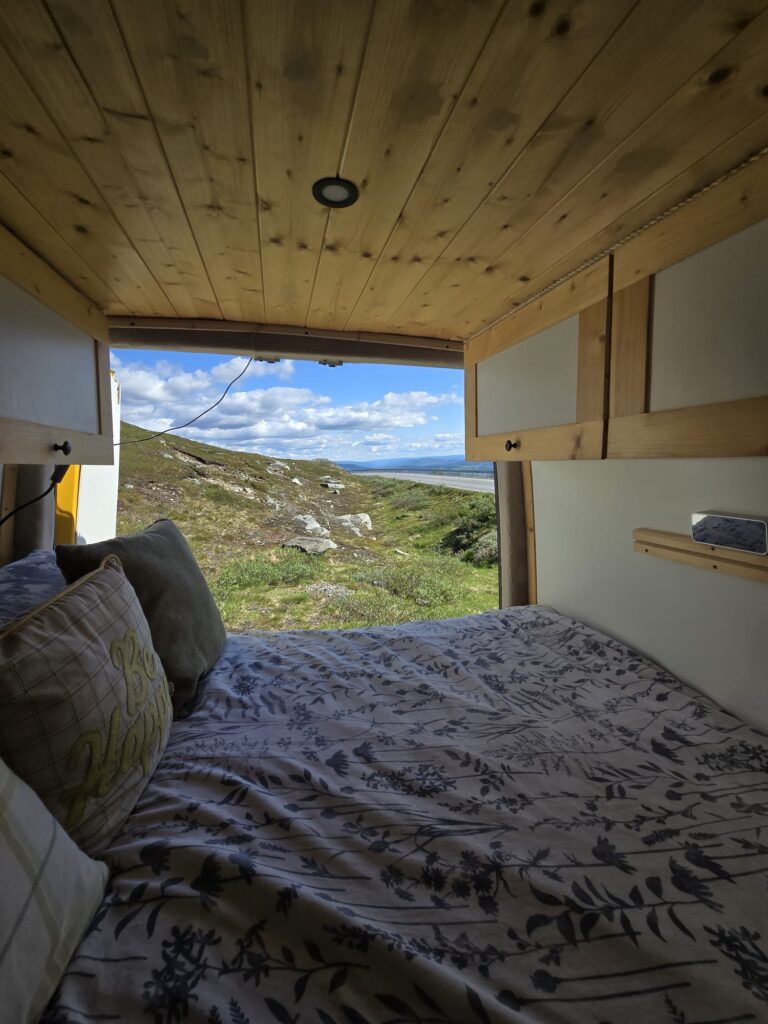 Van Life Europe: Mark, Nikki & Sid’s Journey | Choosing Freedom on the Road 4 Inside Mercedes Sprinter camper van bed with scenic mountain view outside