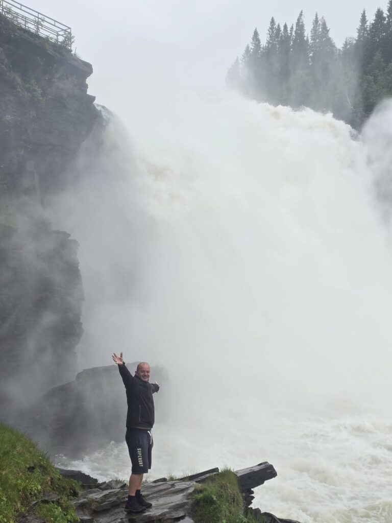 Van Life Europe: Mark, Nikki & Sid’s Journey | Choosing Freedom on the Road 5 Man standing near powerful waterfall in Norway during van life travel